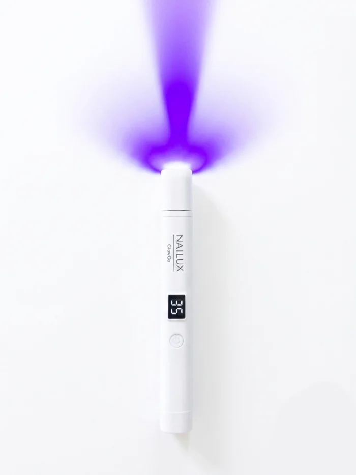 Uključena GlowGo lampa za nokte koja emitira zrake postavljena je na bijeloj pozadini.