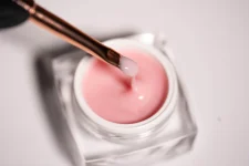 Prozirna bočica s Mousse Gel Blush koja sadrži gradivni gel roze boje. Iznad bočice nalazi se kist kojim se nanosi ovaj gel, koji je prethodno umočen i sa njega curi gel.